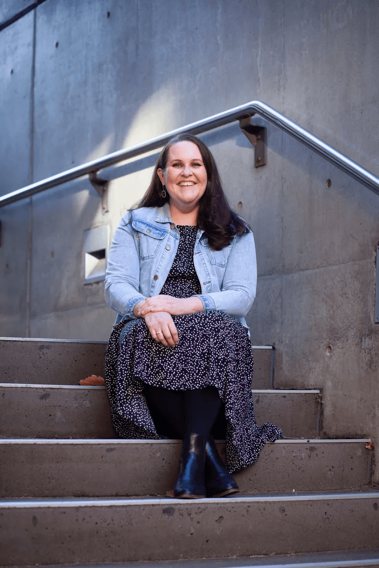 Morwenna Collett, an accessibility expert and partner, seated for a portrait in on concrete steps with a brick wall behind her.