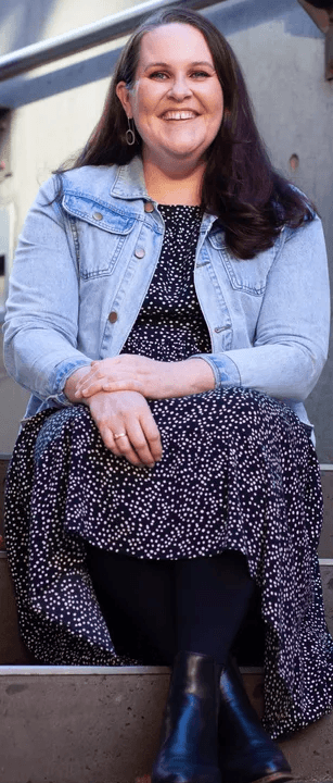 Morwenna Collett, an accessibility expert and partner, seated for a portrait in on concrete steps with a brick wall behind her.